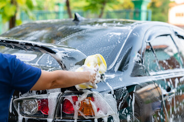 Woman hand hold yellow sponge washing spoiler black car at home.
