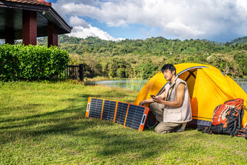 Young travel man relax and enjoy camping . Hand male plug in portable solar panel charging smartphone by multipurpose cable, Clean energy for using in camping or at home when no electricity