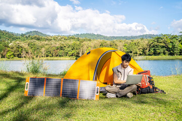Young travel man relax and enjoy camping . Hand male plug in portable solar panel charging laptop...