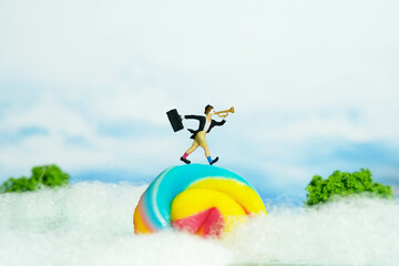Miniature people toy figure photography. Playground island above clouds. A clown wearing black suit and hat blow the trumpet walking above rainbow candy