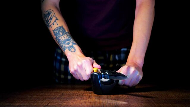 A man sharpens knives on a black background
