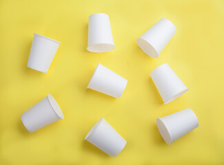 White paper disposable cups on a yellow background. View from above.Flat lay.