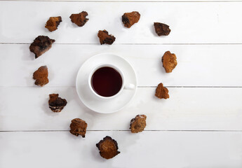 Chaga coffee in a porcelain cup and heart shaped pieces of chaga around on a white wooden background.