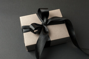 Craft gift box on a dark background, decorated with a textured bow, creating a romantic luxury atmosphere. For birthday, anniversary presents, gift post cards, banner, flyer, invitation, voucher - 553899064