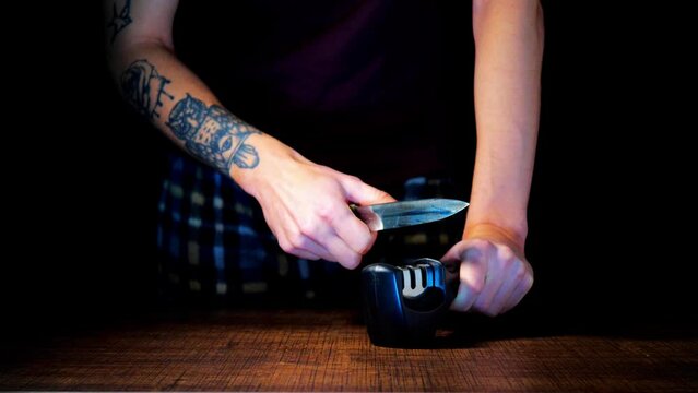 A man sharpens knives on a black background