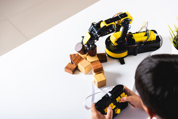 Happy Asian little kid boy using remote control playing robotic machine arm for pick up wood block, Funny child learning successful getting lesson control robot arm, Technology science education