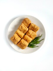 Fried tofu called tahu pong and green chili peppers placed on a ceramic plate isolated on white background. Tahu pong is a type of tofu, popular in Indonesia
