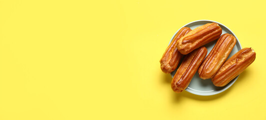 Plate of sweet tasty eclairs on yellow background with space for text, top view
