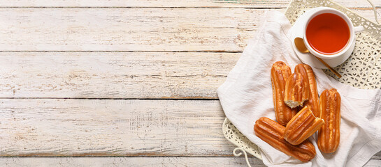 Tray with sweet tasty eclairs and hot tea on light wooden background with space for text, top view