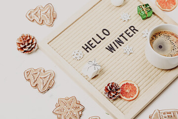 Lettering hello winter on letter board. Fir branches, dried oranges, nuts and a cup of coffee. minimalistic new year background 2023