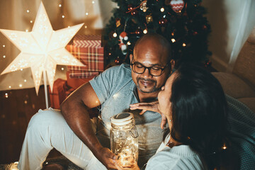 Happy interracial couple celebrating New Year at home together, sitting by Christmas tree