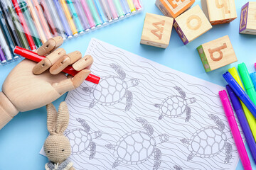Coloring page, felt-tip pens, pencils, wooden hand and toys on blue background