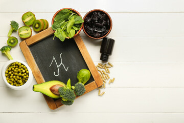 Chalkboard with letter K, healthy products and bottle of pills on white wooden background
