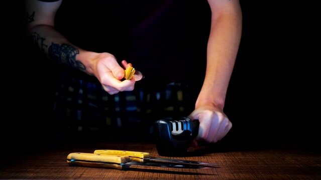 A man sharpens knives on a black background