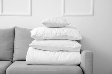 Folded white blanket with pillows on sofa near light wall