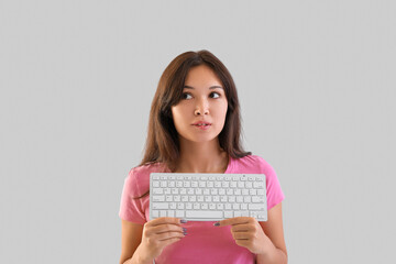 Thoughtful young Asian woman with computer keyboard on light background