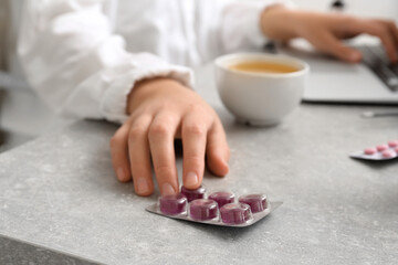 Woman taking pills for sore throat from table in office, closeup