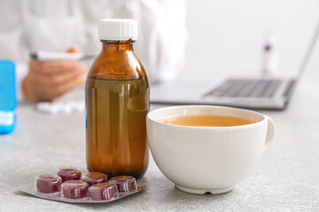 Cup of tea, pills for sore throat and cough syrup on table in office, closeup