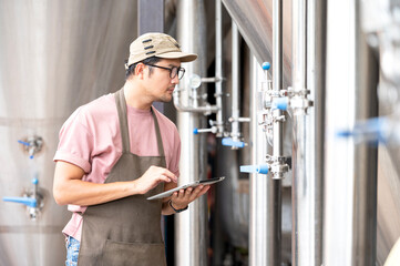 Young Asian worker inspecting brewery quality with a glass of craft beer evaluating visual...