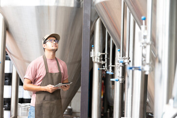 Young Asian worker inspecting brewery quality with a glass of craft beer evaluating visual...