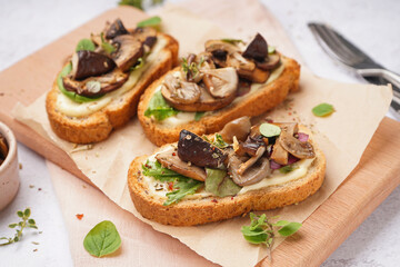 Wooden board of tasty toasts with cream cheese and mushrooms on light background, closeup