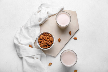 Board with glasses of healthy almond milk and nuts on light background