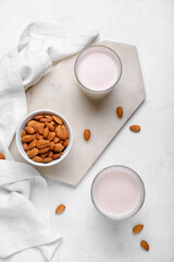 Board with glasses of healthy almond milk and nuts on light background