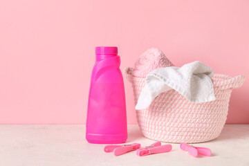 Laundry detergent, clothespins and basket on table against pink background