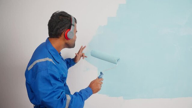 Enjoying painter listening songs on headphones by dancing while working at apartment - concept of entertainment, maintenance service and relaxation.