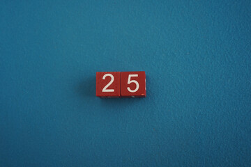 Wooden Viva Magenta cubes with number 25 blue background close-up top view. Concept of date or time. White numbers 25 on red cubes velvet background. Copy space for text or event. Blurred background