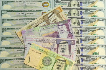 Saudi Arabia riyal banknotes over a US 100 dollar bills closeup