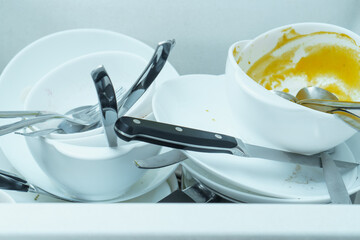 Close-up of sink full of dirty white tableware, plates, bowls, knives, forks, spoons. Cooking, housekeeping, cleaning.
