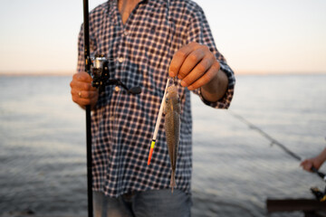 Success fishing. fisherman with fishing rod and small fish trophy at lake
