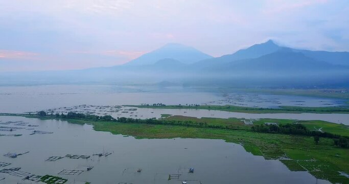 Aerial view of lake with green rice field and mountain range on the background - Rawa Pening Lake, Indonesia