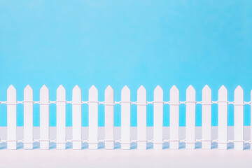 Wooden vintage white picket fence on blue background. Low rustic closed boundary design element,...