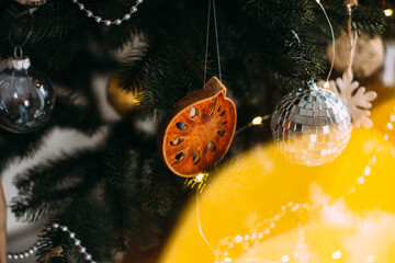 Christmas tree with festive lights, decorated with a piece of dried orange and wooden figurines, close-up.