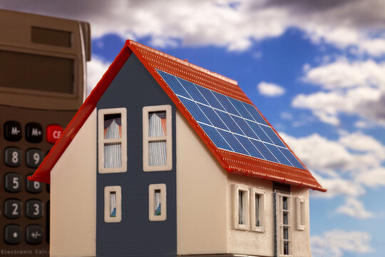 Symbolbild Kosten für eine Photovoltaikanlage: Modellhaus und Taschenrechner vor einem blauen Himmel