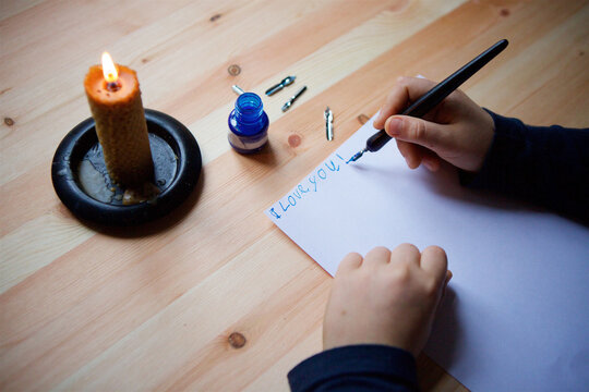Children's hands write letters on white paper with an ink pen.