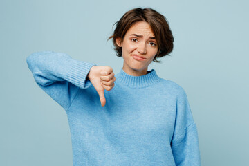 Young sad unhappy caucasian woman wearing knitted sweater look camera showing thumb down dislike...