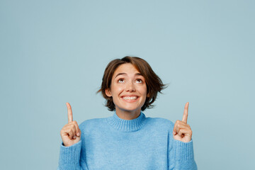 Young woman in knitted sweater point index finger overhead indicate on workspace area copy space mock up isolated on plain pastel light blue cyan background studio portrait. People lifestyle concept