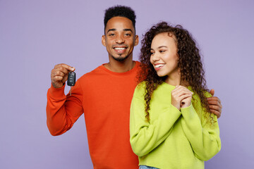 Young smiling couple two friends family man woman of African American ethnicity wear casual clothes together hold in hand car key fob keyless system misolated on pastel plain light purple background.