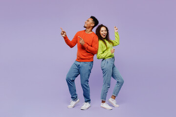 Full body sideways fun young couple two friends family man woman of African American ethnicity wear casual clothes together point finger aside on area isolated on pastel plain light purple background.
