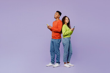 Full body side view young couple two friends family man woman of African American ethnicity wear casual clothes together hold use mobile cell phone look overhead isolated on plain purple background.