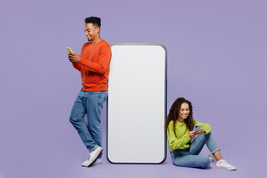 Full body young couple two friends family man woman wear casual clothes together sit big huge blank screen mobile cell phone with area use smartphone isolated on pastel plain light purple background.