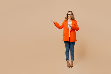 Full body young employee business woman corporate lawyer wears classic formal orange suit glasses work in office point index finger aside on workspace area isolated on plain beige background studio.