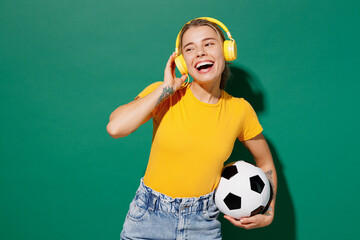 Young woman fan in basic yellow t-shirt headphones cheer up support football sport team hold in...