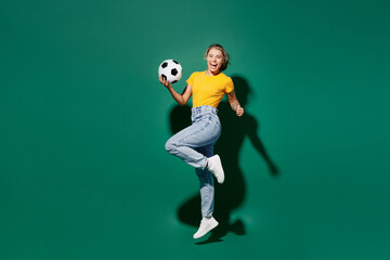 Fototapeta na wymiar Side view full body young woman fan in basic yellow t-shirt cheer up support football sport team hold in hand soccer ball watch tv live stream jump high clench fist isolated on dark green background