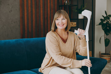 Elderly sick ill smiling woman 50s year old wears casual clothes sits on blue sofa hold in hand...