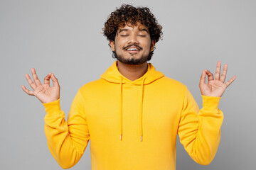 Young spiritual Indian man wear yellow hoody hold spreading hands in yoga om aum gesture relax...