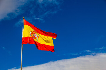 flag of spain red yellow on blue sky background with white clouds